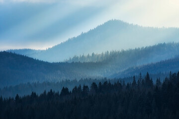 Mountain view on a sunny day. Sunrays from clouds shining down to mountains.  Silhouettes of trees on the mountains.