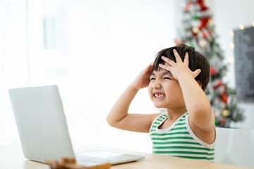 Lovely Asian little boy showing a funny face while studying on laptop computer or notebook. 