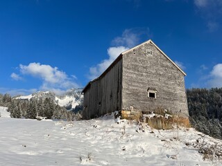 Indigenous alpine huts and wooden cattle stables in the Swiss Alps covered with fresh first snow over the Lake Walen or Lake Walenstadt (Walensee), Amden - Canton of St. Gallen, Switzerland / Schweiz