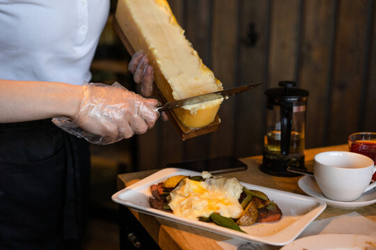 The waiter cuts the cheese into a raclette with a knife
