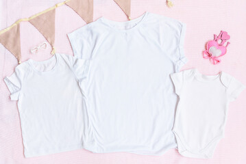Mothers day mom and kids mockup white t-shirt and baby bodysuit onesie with heart on pink cover background. Flatlay, top view, copyspace.