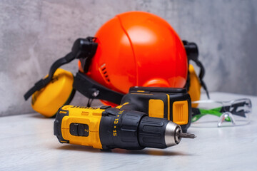 Electric screwdriver and a construction safety helmet for a head with an earpiece and a headlamp on the table. Construction tool and form for protection.