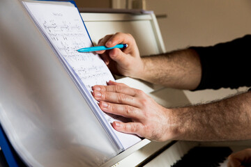 Photographie des mains d'un professeur de piano montrant avec son crayon les notes de musique sur...