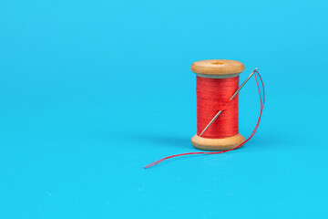 Spool of red thread with a needle on a blue background