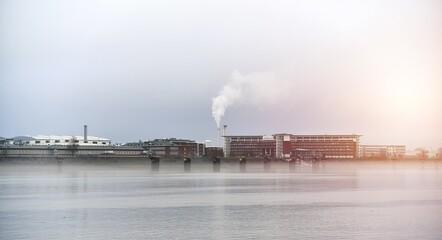 Fototapeta premium Factory over the river. Plant in Germany. Smoke from chimney industrial zone.