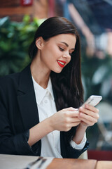 Fashion woman blogger tourist sits in a cafe with a phone in her hands reads a message, mobile communication and internet in travel spring, video call, freelance work online, smile with teeth