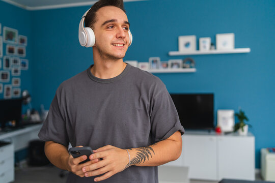 A portrait photos of a young guy listening to music on his wireless headphones and taking selfies with headphones while listening to music in his house during the day