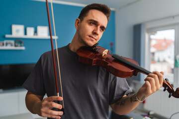 A portrait of a young guy playing or learning a violin in his home private classes online course...