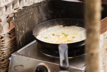 egg omelette is made in a frying pan on the streets of kolkata. it is a very popular early morning breakfast street food made with green chilli and onion.