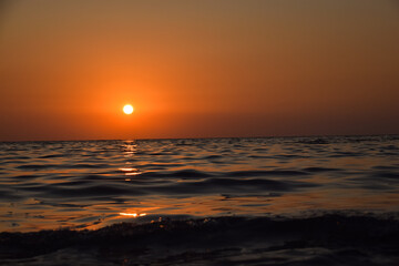 Vibrant sunset descending on the horizon, sea in golden colors, small waves gently touching the...