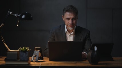 Businessman sitting at desk with laptop computer. Entrepreneur working late in office. Older, middle aged, mid adult, man in his 40s or 50s in jacket, business casual.