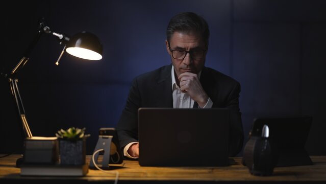 Businessman sitting at desk with laptop computer. Entrepreneur working late in office. Older, middle aged, mid adult, man in his 40s or 50s in jacket, business casual.