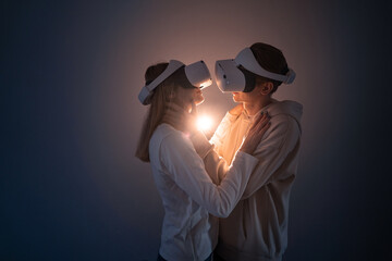 Virtual reality lovers. Young gamers couple hugging kissing wearing VR headset. Romantic virtual world. Warm light of hope between them Dark colors horizontal conceptual composition. Digital closeness