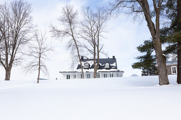 Pretty low angle landscape with patrimonial presbytery on snowy hill surrounded by bare trees in the Cap-Rouge area of Quebec City during a winter day, Quebec City, Quebec, Canada