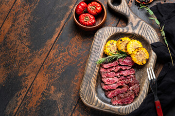 grilled flank steak cut on a board with fried corn, top view and copy space