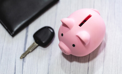 Um cofrinho sobre uma mesa de madeira com a chave de um carro na composição. Guardar dinheiro para comprar um carro ou para fazer a manutenção do veículo. Dinheiro, Guardar Dinheiro, Automotivo.