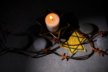 Holocaust memory day. Barbed wire, stones, yellow star and burning candle on black background