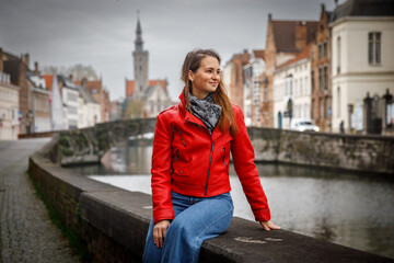 Traveling old Europe. Beautiful woman as a tourist in Brugge, Belgium in the red jacket in autumn.