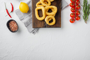 Fried squid rings breaded calamari appetizer, on serving board, on white stone table background,...