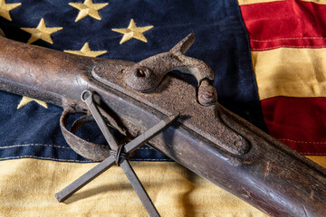 old rusted musket gun and metal cross on tea stained American flag