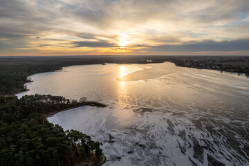 Fototapeta na wymiar Golden hour over the frozen lake. Golden sunset over the frozen lake. Sunset reflection in water. Winter sunset over lake.