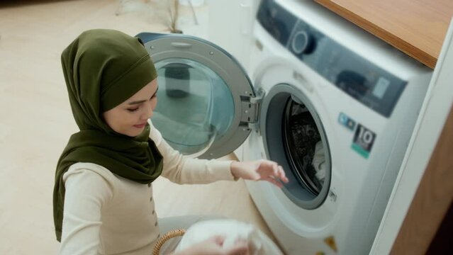 Happy young muslim woman wearing hijab doing laundry in home , healthy lifestyle concept