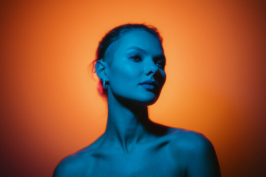 Fashion woman profile portrait on orange gradient background with soft blue light play on skin and copy space. Lights play.