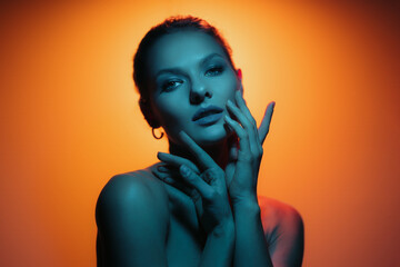Fashion woman profile portrait on orange gradient background with soft blue light play on skin. Hands touching skin. Lights play.
