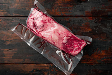 Raw rib eye beef meat steak cut in vacuum packaging, on old dark  wooden table background, top view flat lay, with copy space for text