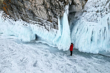 A female traveler stands by ice and snow rocks with huge icicles. Winter trip on the frozen lake Baikal. Aerial view.