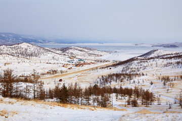 Beautiful view of the coast of the Small Sea of Lake Baikal, Kurkut Bay, tourist camps and wooden hotel houses. Winter landscape