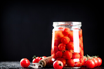 Pickled tomatoes in a glass jar on the table. 
