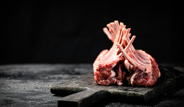 Raw rack of lamb on a cutting board on the table. - Powered by Adobe