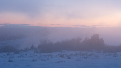 Warm pink light on the horizon mixes  with cold blue light in this foggy, snowbound, winter landscape just after the sun has set in the mountains of Southern Utah, USA near Zion National park.