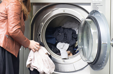 middle-aged woman in black dress and brown jacket, using self-service laundromat, introducing dirty clothes and using card payment, horizontal image, copy space