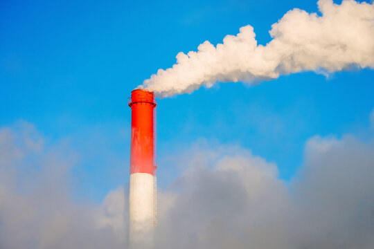 Red pipe of a plant with exhaust  white smoke, blue sky among smog.