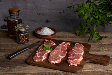 Iberian pork loin steaks on a cutting board, on a rustic old wooden table with olive oil, peppercorns and coarse salt, ready to cook.