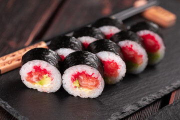 Maki sushi roll with salmon avocado and tobiko caviar served on black board close-up - Japanese food