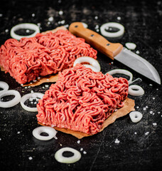 Fresh minced meat on paper on a table with a knife and onion rings.