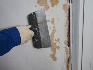  worker's hand in a glove with a spatula removes old plaster from the wall