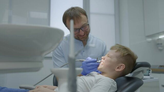 Professional male dentist with glasses drills the teeth of little boy. Little boy at dentist. Slow motion