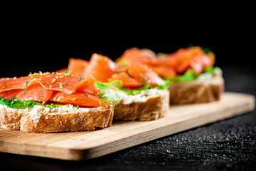 Sandwich with pieces of salmon on a cutting board. 