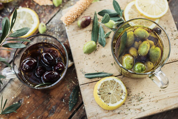 Various olives flavored with spices in cup and glass jar. Green olives, black olives. Front and top shot on wooden floor