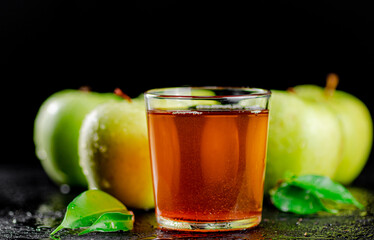 A glass of green apple juice with leaves on the table. 