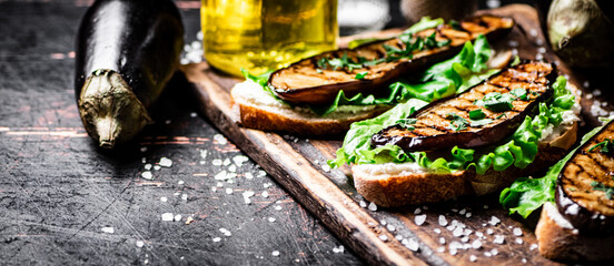 Sandwich with grilled eggplant and lettuce on a wooden cutting board. 