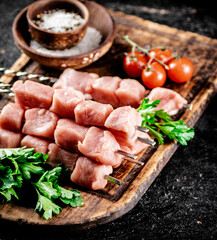 Pork kebab raw on a cutting board with tomatoes and parsley. 