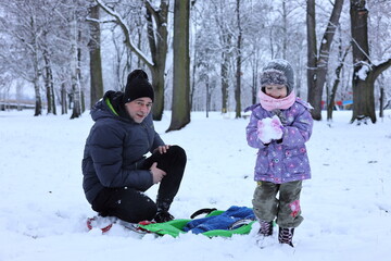Happy little child and father enjoying the time on sled. A little girl play snowballs. Activity for winter holidays