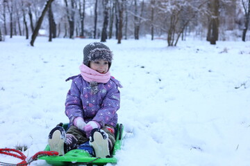 Fototapeta na wymiar Happy little child enjoying the time on sled. A little girl rides a bobsleigh. Activity for winter holidays