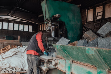 A worker in heavy industry breaks stone blocks using large machines. Granite and stone processing industry.