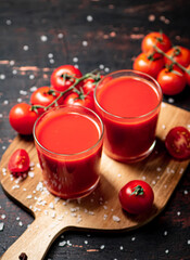 Tomato juice in glasses on a wooden cutting board. 